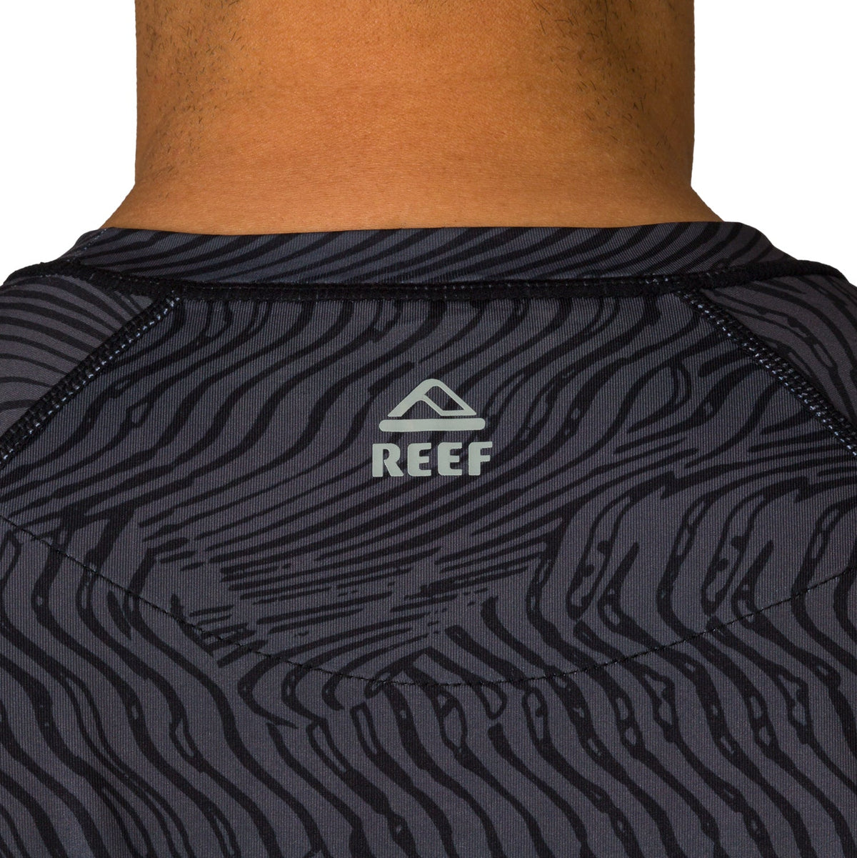 Close-up of the back neck area of the men's Dune Performance Shirt with surf-inspired dark patterned fabric and REEF logo.