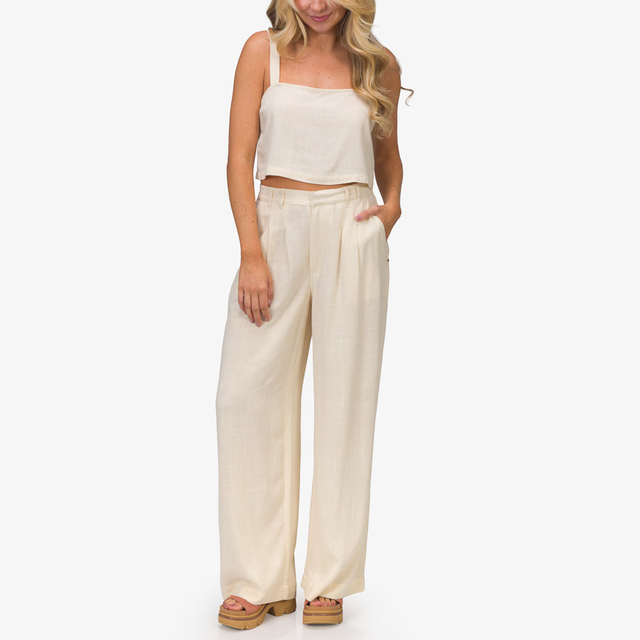 Woman wearing Tori Linen Tank in almond milk, standing with relaxed pose, showcasing beach-inspired, comfortable apparel.